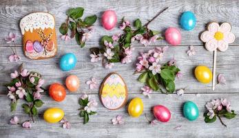 osterfestes layout aus rosa apfelbaumzweigen, wachteln und bemalten hühnereiern, mehrfarbigen lebkuchen auf holztisch. foto