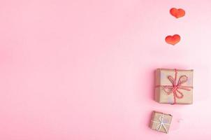 zwei trendige diy verpackte geschenkboxen und zwei rote herzen auf rosa hintergrund. valentinstag festliches flaches lag-modell. foto