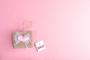 kleine dekorative Weidenhandtasche und weiße Papierkarte mit Worten Verkauf auf rosa Hintergrund. Valentinstag-Verkaufskonzept. foto