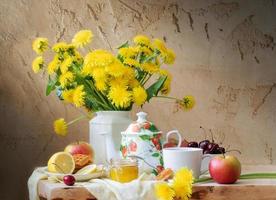 stillleben mit löwenzahn, wasserkocher, obst und honig auf holztisch auf altem rissigem hintergrund. foto