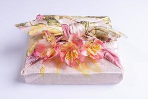 Nahaufnahme trendig verpackt in floralem Textil in Furoshiki-Technik Geschenkbox mit Blumen Alstroemeria auf grauem Hintergrund. foto