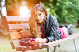 Mädchen auf einer Bank schreibt er auf sein Smartphone foto