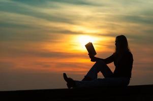 Mädchen, das bei Sonnenuntergang ein Buch an der Wand liest foto