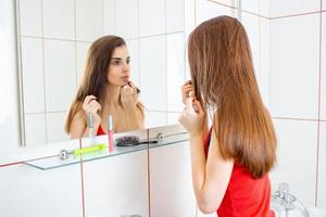 dlinnnymi ist ein wunderschönes mädchen mit dunklen haaren, sieht in den spiegel und malt lippen lippenstift foto