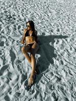 junge dame des zaubers, die auf weißem sand bei heiß ein sonnenbad nimmt foto