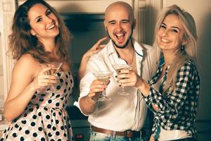 Zwei Mädchen haben Spaß mit einem Mann auf einer Party bei einem Glas Martini foto