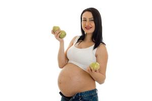 Happy brunette schwangere Frau posiert mit grünem Apfel in ihren Händen und lächelt vor der Kamera isoliert auf weißem Hintergrund foto