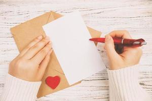 Hand eines Mädchens, das am Valentinstag einen Liebesbrief schreibt. handgefertigte Postkarte getönt, Vintage. frau schreibt auf postkarte für feiertagsfeier am 14. februar. flach liegen. Ansicht von oben foto