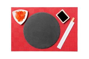 leerer runder schwarzer Schieferteller mit Essstäbchen für Sushi und Sojasauce, Ingwer auf rotem mattem Sushi-Hintergrund. Draufsicht mit Kopierbereich für Ihr Design foto
