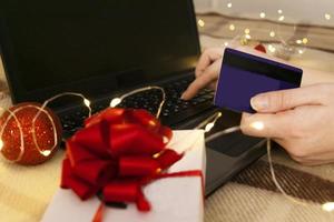 weiße geschenkbox mit roter schleife und laptop mit weihnachtslicht foto