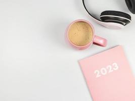 rosa tagebuch 2023, kopfhörer und rosa tasse kaffee auf weißem hintergrund. foto