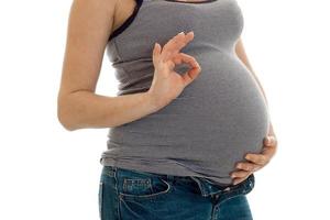 junge schwangere brünette Frau mit dickem Bauch posiert und zeigt OK-Symbol isoliert auf weißem Hintergrund foto