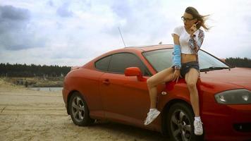 Wunderschöne Blondine mit Brille sitzt auf einem roten Auto mit Lutscher in den Händen foto