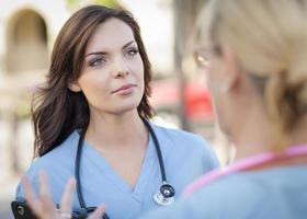 Zwei junge erwachsene Ärztinnen oder Krankenschwestern sprechen draußen foto
