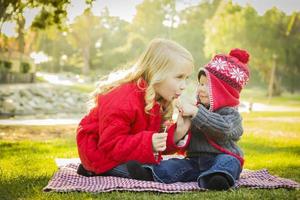 kleines Mädchen mit kleinem Bruder, der im Freien Mäntel und Hüte trägt foto