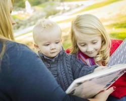 Mutter, die ihren beiden entzückenden blonden Kindern ein Buch vorliest foto