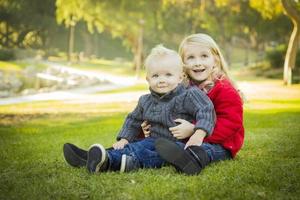kleines Mädchen mit kleinem Bruder, der Mäntel im Park trägt foto