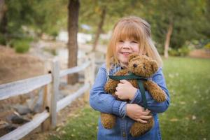 süßes lächelndes junges mädchen, das draußen ihren teddybär umarmt foto