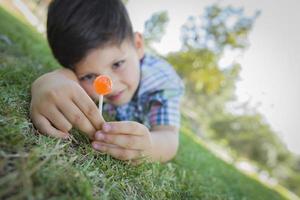 kleiner Junge genießt seinen Lutscher im Freien, der auf Gras liegt foto