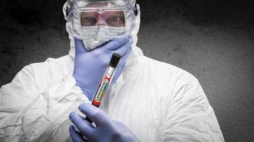 männlicher Arzt oder Krankenschwester in Hazmat-Ausrüstung mit positivem Coronavirus-Reagenzglas foto