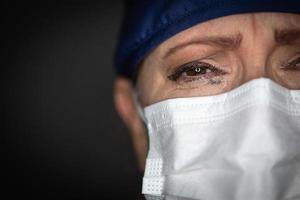 tränenreiche gestresste Ärztin oder Krankenschwester mit medizinischer Gesichtsmaske auf dunklem Hintergrund foto