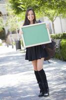 Aufgeregte gemischtrassige Studentin, die eine leere Tafel hält foto