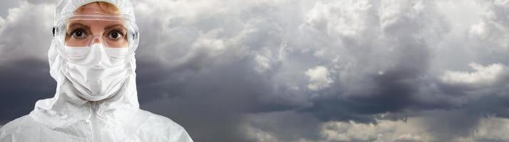 weibliches medizinisches Personal, das eine schützende Gesichtsmaske und Ausrüstung gegen bewölkten, stürmischen Himmel trägt foto