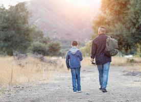 Vater und Sohn gemischter Rassen im Freien, die mit Angelruten spazieren gehen foto