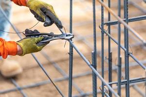 Arbeiter, der Stahlbewehrungsrahmen mit einem Drahtzangen-Schneidwerkzeug auf der Baustelle sichert foto