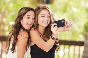 zwei attraktive Freundinnen gemischter Rassen, die ihre Smartphones für Selfies im Freien benutzen foto