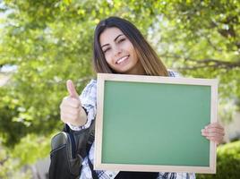 Aufgeregte gemischtrassige Studentin, die eine leere Tafel hält foto