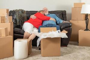 liebevolles müdes älteres erwachsenes Paar, das auf der Couch ruht, umgeben von Umzugskartons foto