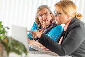 Frau, die älterer erwachsener Dame auf Laptop-Computer hilft foto