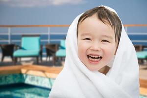 Fröhlicher, süßer, gemischtrassiger chinesischer und kaukasischer Junge auf einem Kreuzfahrtschiff, eingewickelt in ein Handtuch foto