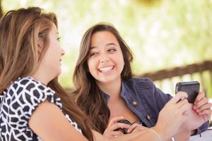 Ausdrucksstarke junge erwachsene Freundinnen, die ihr Smartphone im Freien benutzen foto