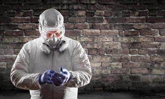 Mann mit Hazmat-Anzug, Schutzgasmaske und Schutzbrille gegen Ziegelwand foto