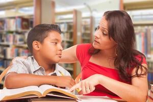 hispanischer kleiner Junge und famle Erwachsener, der in der Bibliothek studiert foto