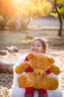 süßes junges gemischtes rassenmädchen, das teddybär im freien umarmt foto