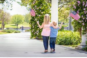 junge schwester und bruder schwenken amerikanische flaggen im park foto