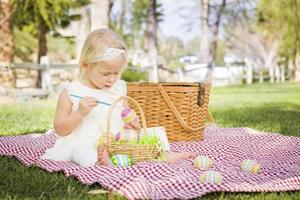 süßes kleines Mädchen, das Ostereier auf der Picknickdecke färbt foto