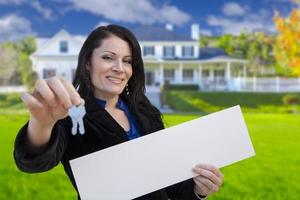 Frau mit leerem Schild und Schlüsseln vor dem Haus foto