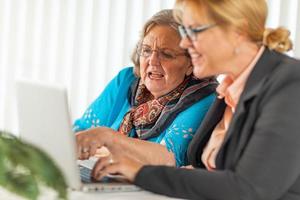 Frau, die älterer erwachsener Dame auf Laptop-Computer hilft foto