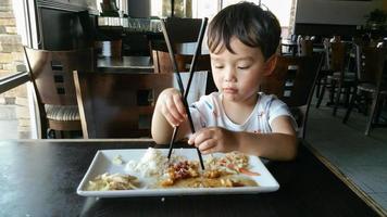 süßer junger chinesischer und kaukasischer junge, der lernt, stäbchen im restaurant zu benutzen foto
