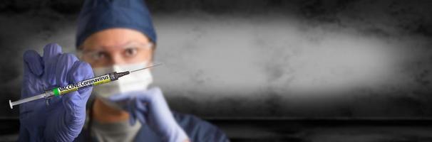 arzt oder krankenschwester, die einen chirurgischen handschuh tragen, der eine medizinische spritze mit dem banner des coronavirus covid-19-impfetiketts hält foto