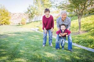 glückliche chinesische großeltern, die draußen spaß mit ihrem enkel gemischter rassen haben foto