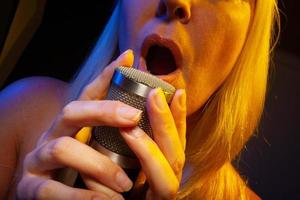 Sängerin unter Gellicht singt mit Leidenschaft in ein Kondensatormikrofon. foto
