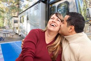 glückliches multiethnisches kaukasisches und hispanisches Paar vor ihrem schönen Wohnmobil auf dem Campingplatz. foto