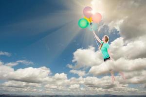 junge erwachsene Frau, die von Ballons, die sie hält, hoch und weg in die Wolken getragen wird. foto