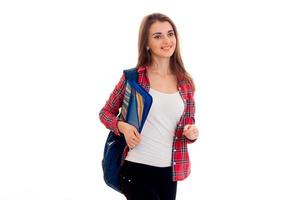 Ein junges Mädchen in einem rot karierten Hemd und mit einer Mappe auf den Schultern steht seitlich und lacht foto