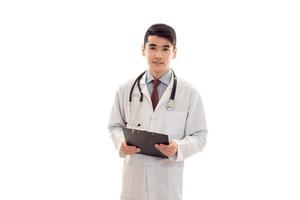 Porträt eines hübschen jungen brünetten männlichen Arztes in Uniform mit Stethoskop, der isoliert auf weißem Hintergrund posiert foto